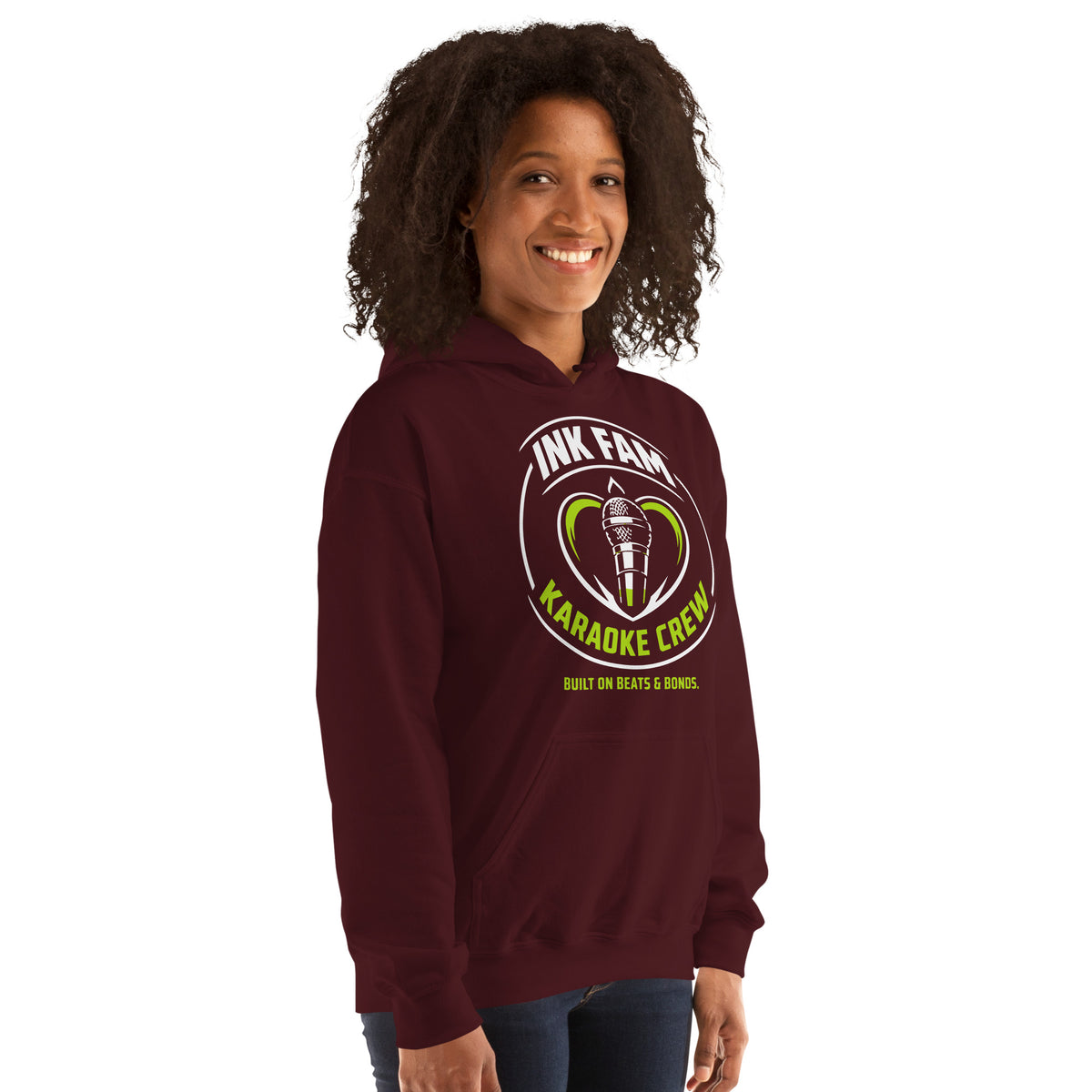 Maroon pullover hoodie, right-front angled view, featuring the green-and-white circular DJ Ink Fam microphone badge.