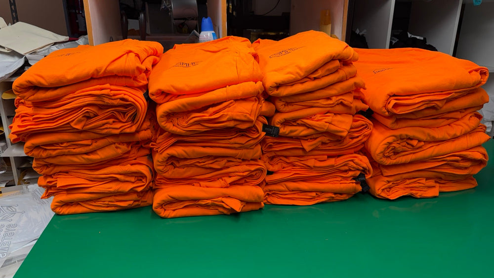 Stacks of completed bright orange company-logo shirts, folded in bundles for Seizmic’s order of 125 shirts.